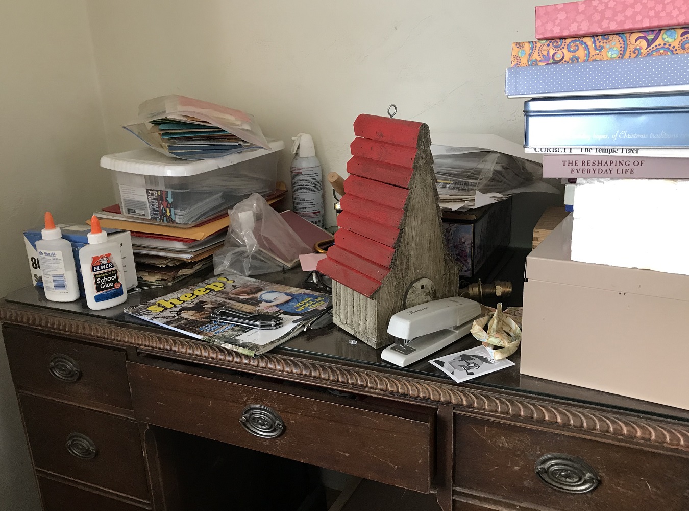 Photo of desk covered with stationary, a stapler, bird house, magazine, books, and other random items.